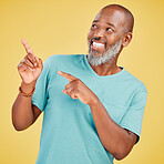 Mature african man smiling and pointing in a direction against a yellow studio background. Black guy looking happy and making a pointing gesture reacting with a smile while looking cheerful and happy. Stay positive you never know what's coming next