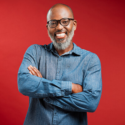 One mature African American man with his arms crossed isolated against a red studio background. Portrait of smiling black man wearing glasses and posing. Confident fashionable man with a grey beard