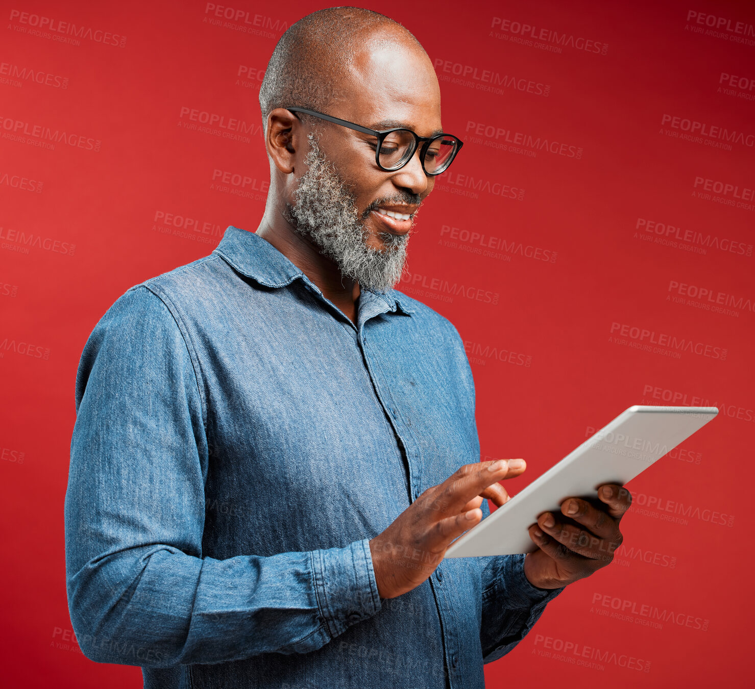 Buy stock photo One happy mature african american man isolated against a red background in a studio and browsing the internet on a digital tablet. Smiling black man using glasses to read social media and new trends