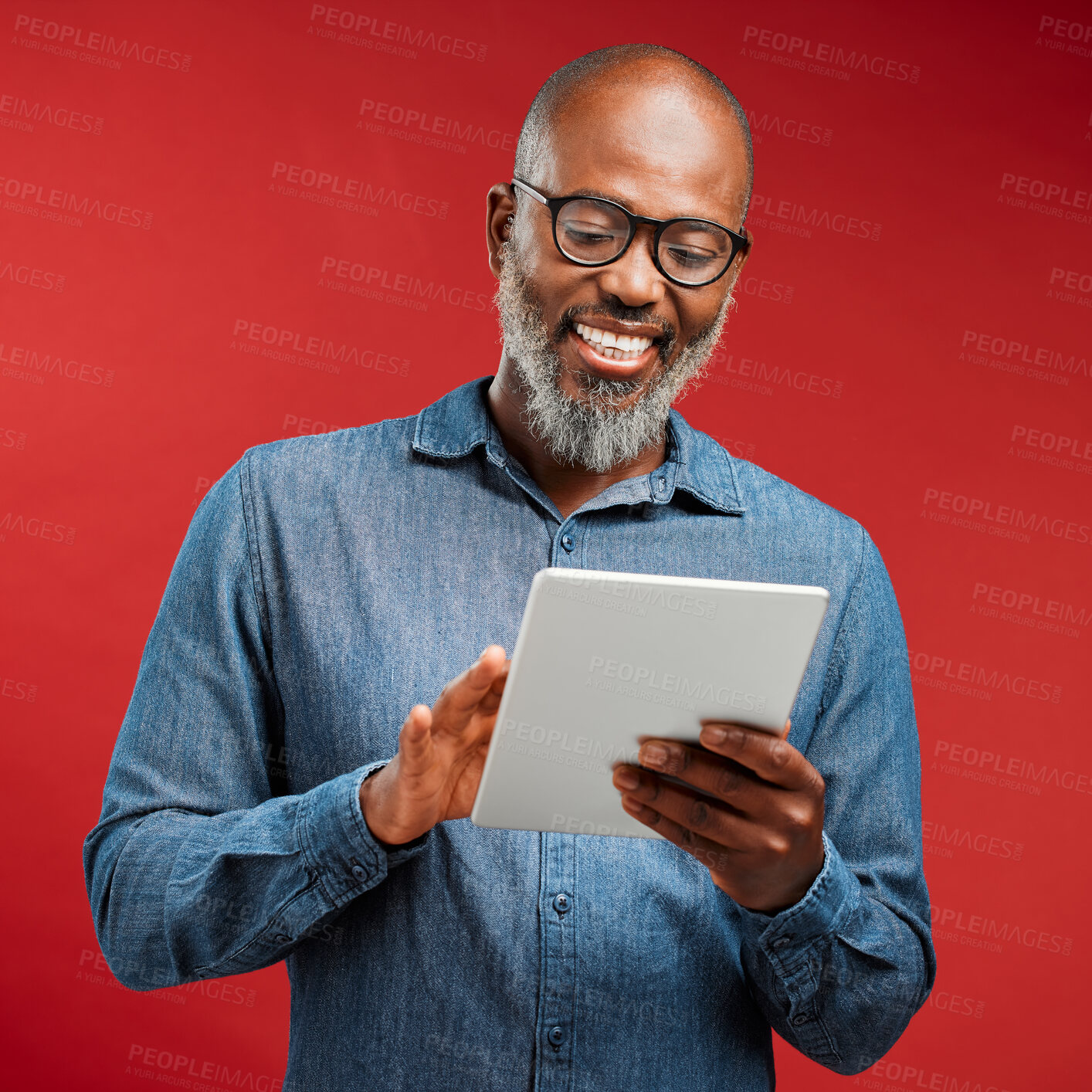 Buy stock photo Smiling man browsing on a tablet online, networking on the internet and scrolling on an app while standing against a red studio background. Happy, mature and African male reading an email and typing