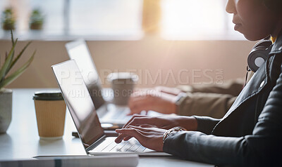 A focused young businesswoman typing on her laptop and wearing headphones. A young african american businesswoman working on her laptop next to a colleague. A businesswoman typing emails on her laptop