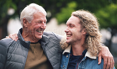 Buy stock photo A mature man hugging his young son during a day in the park. A cheerful young man relaxing in the park with his father. A senior man with his arm around his son walking through the park