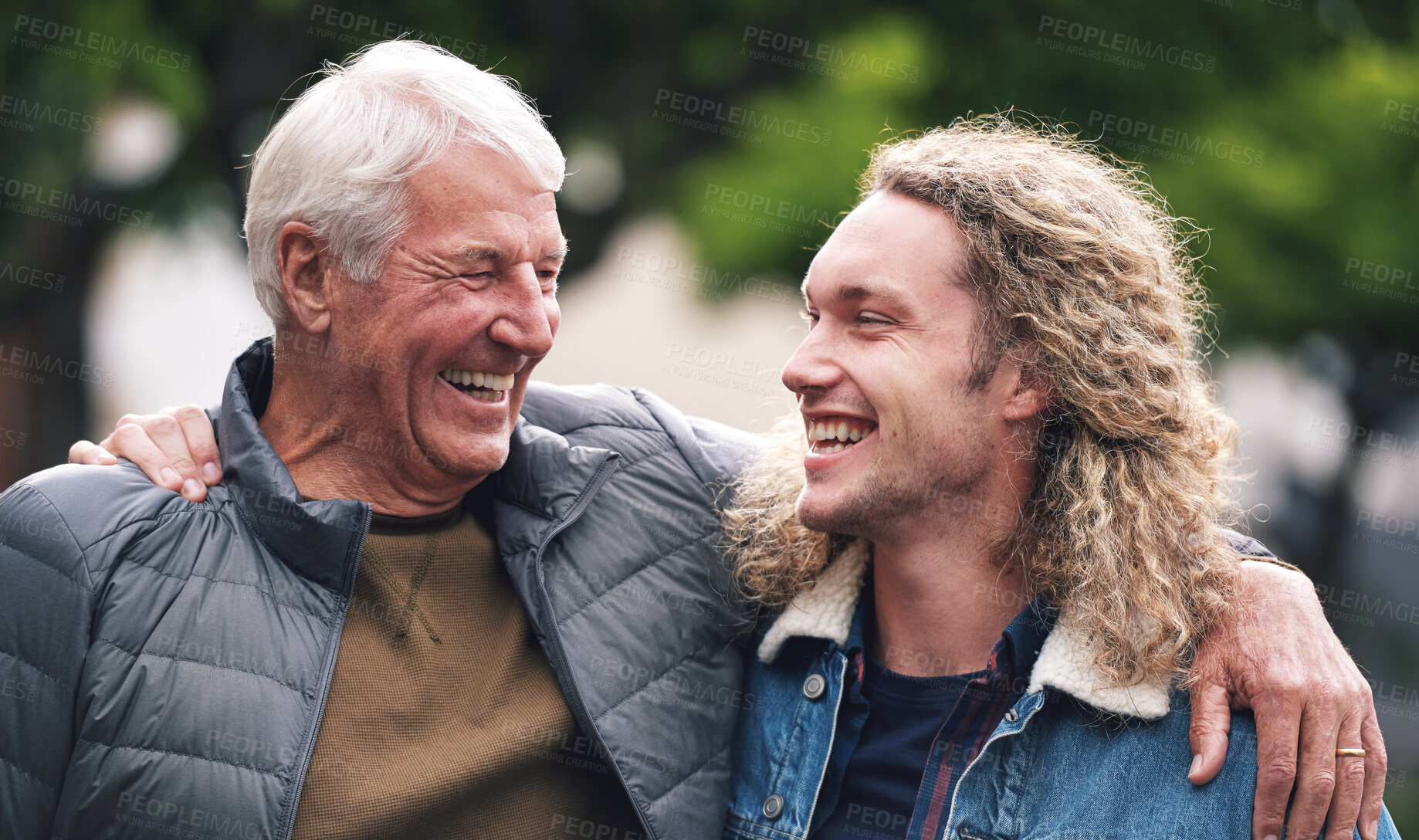 Buy stock photo A mature man hugging his young son during a day in the park. A cheerful young man relaxing in the park with his father. A senior man with his arm around his son walking through the park