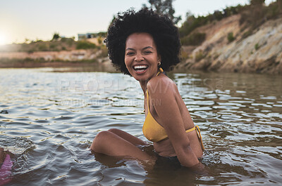 Buy stock photo Portrait of cheerful African american woman with afro wearing a bikini while sitting in water outdoors. Carefree woman having fun while out for a swim at the lake 