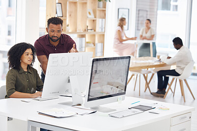 Two happy mixed race businesspeople working on a computer in an office at work. Cheerful hispanic colleagues using a desktop computer together. Businessman helping a female coworker at work