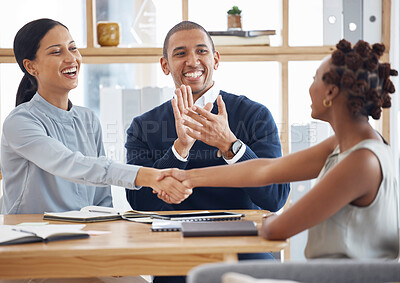 Cheerful female coworkers shaking hands while their male mixed race colleague claps hands. Group of diverse businesspeople having a meeting at a table in an office. Hispanic boss promoting an employee
