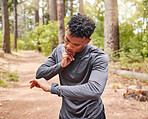 Sporty man looking at his smart watch and checking his pulse while our for a run or jog through the woods. Fit and healthy man exercising in nature environment
