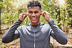 One active young man listening to music with earphones while exercising at the park. Confident mixed race athlete staying motivated with songs from playlist for a run or jog in the morning outside