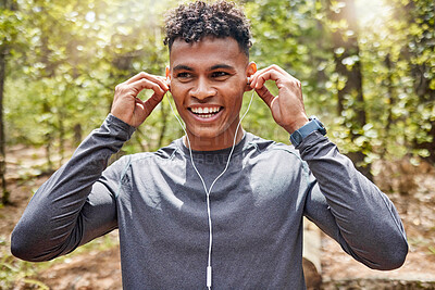 Buy stock photo One active young man listening to music with earphones while exercising at the park. Confident mixed race athlete staying motivated with songs from playlist for a run or jog in the morning outside