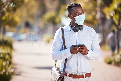 Buy stock photo One handsome african american man wearing a mask to protect himself from the corona virus pandemic while wearing headphones around his neck and texting on a phone. A young business man walking outside