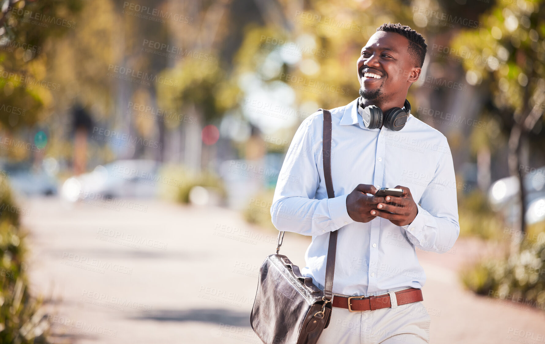 Buy stock photo Happy african american businessman wearing headphones and texting on a cellphone while commuting in the city. One young black guy looking thoughtful while using apps and browsing social media online