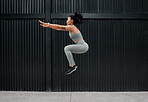 One sporty young african american woman jumping while exercising outside. A beautiful brunette mixed race female athlete working out in the city. Dedicated to fitness and living a healthy lifestyle