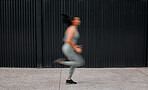 Dedicated young african american sportswoman running outside in blurred motion through the city. Athletic mixed race woman working out, focusing on cardio and endurance while jogging outside