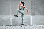 One young mixed race female athlete running on the spot while exercising outside in the city. Beautiful and dedicated  sportswoman working out alone against an urban background