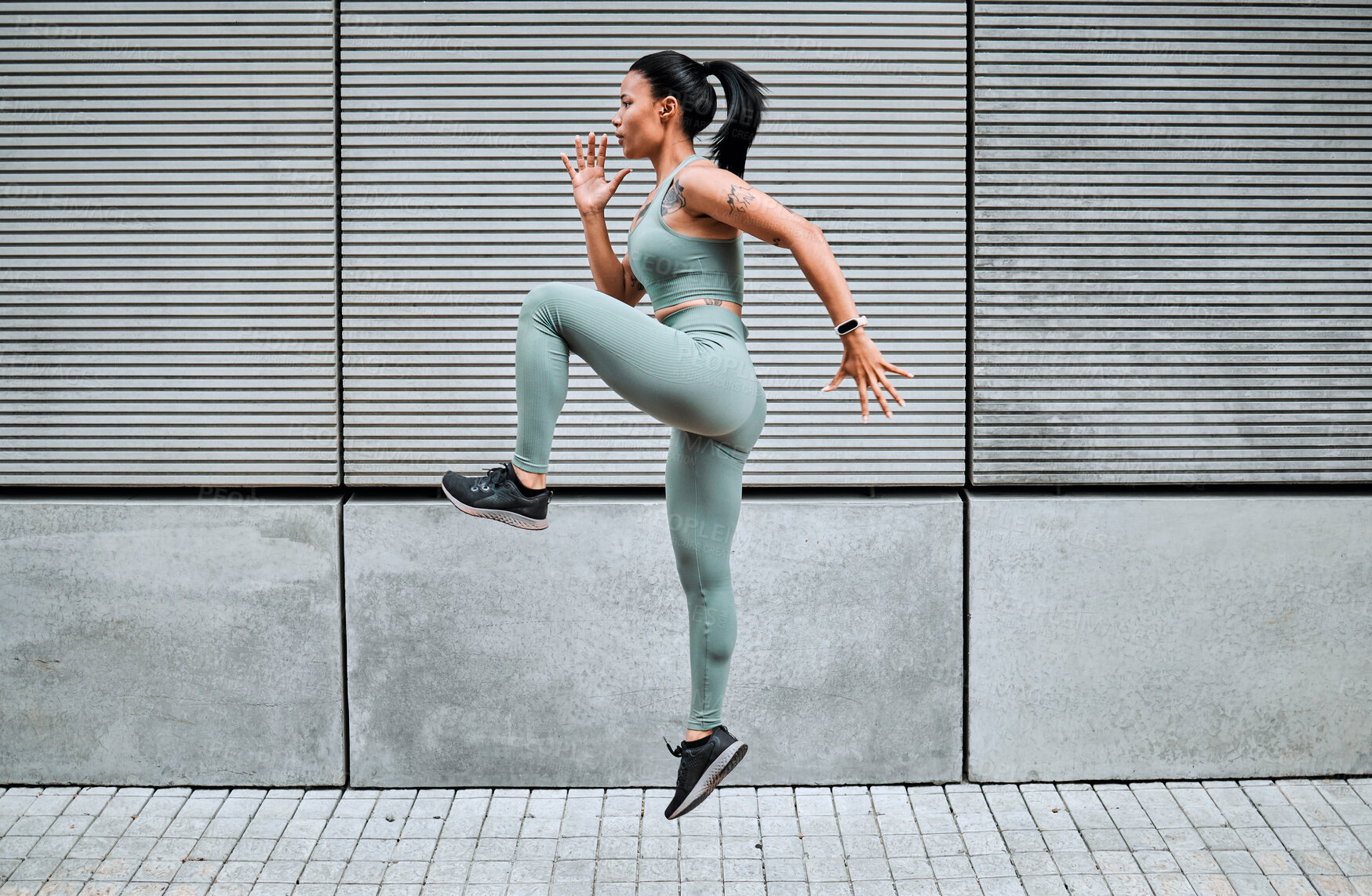Buy stock photo One young mixed race female athlete running on the spot while exercising outside in the city. Beautiful and dedicated  sportswoman working out alone against an urban background