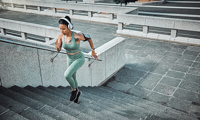 Buy stock photo Young mixed race female athlete wearing gymwear and headphones while running up the steps of a building outside. Young sportswoman focused on her speed, body, fitness and cardio health while training