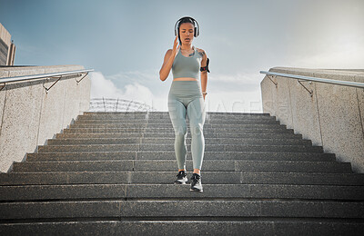Young mixed race female athlete listening to music on headphones while running down the steps of a building outside. Young female focused on her speed, body, fitness and cardio health while training