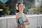 Young mixed race female athlete wearing headphones armband while listening to music  and standing with her arms crossed exercising outside in the city. Positive, happy, workout
