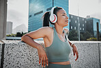Young mixed race hispanic female athlete wearing headphones and listening to music while standing outside in the city. Positive, happy, workout. Taking a break