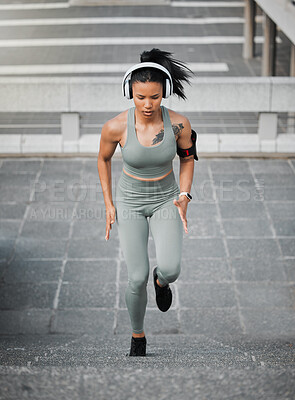 Young mixed race female wearing gym wear and wireless headphones while running up the steps of a building outside. Young female focused on her speed, body, fitness and cardio health while training