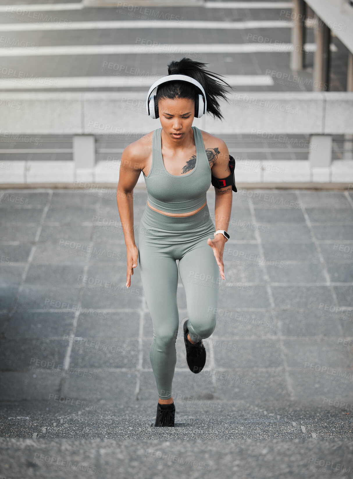 Buy stock photo Young mixed race female wearing gym wear and wireless headphones while running up the steps of a building outside. Young female focused on her speed, body, fitness and cardio health while training