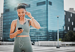 Fitness woman looking happy and smiling while wearing earphones and listening to music from a cellphone while reading a text message in the city. Woman enjoying a break from exercising outside.