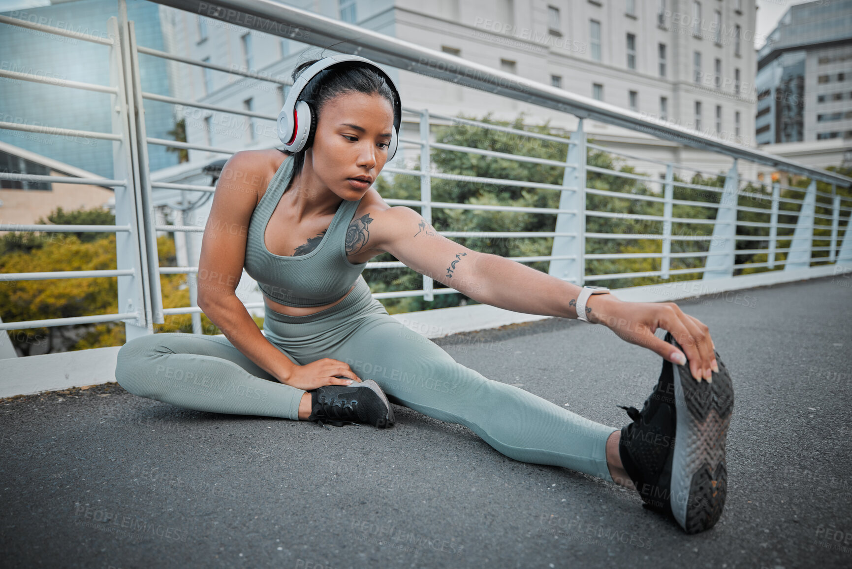 Buy stock photo Young mixed race female athlete wearing headphones and listening to music while stretching before a run outside In the city. Confident hispanic sportswoman warming up before starting her exercise
