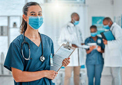 Buy stock photo Mixed race female doctor holding a clipboard and wearing a mask while working at a hospital with colleagues. Hispanic expert medical professional ready for work at a clinic with coworkers