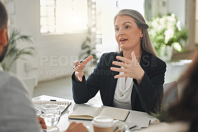 Businesspeople talking in a meeting together at work. Business professionals talking and planning in an office. Mature caucasian businesswoman explaining an idea to colleagues at a table
