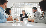 Mature caucasian businesswoman explaining an idea in a meeting at work. Group of businesspeople having a meeting together at a table. Business professionals talking and planning in an office