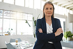Mature focused caucasian businesswoman standing with her arms crossed while in an office alone. One confident female manager standing at work