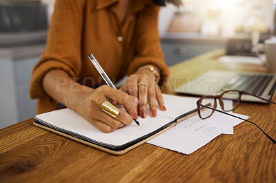 Mixed race businesswoman writing in a notebook while working from home. One hispanic female businessperson taking notes and planning in a diary