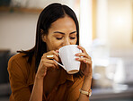 Young happy beautiful mixed race woman enjoying a cup of coffee alone at home. Hispanic female in her 20s drinking a cup of tea in the kitchen at home
