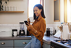 Young happy mixed race woman drinking a cup of coffee while using her phone alone in the morning in the kitchen. One hispanic female smiling and enjoying a cup of tea while using social media on her phone at home