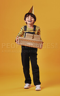 An adorable little Asian boy holding presents and looking happy while wearing a fun party hat against an orange copyspace background. Excited child at a party