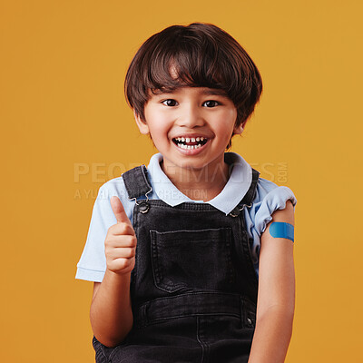 Portrait of a smiling happy mixed race child giving the thumbs up to the vaccine while showing his bandaid and posing against an orange copyspace background