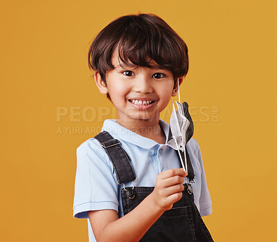 Portrait of an adorable little Asian boy happy while wearing a mask against an orange studio copyspace background. Smiling kid removing his mask