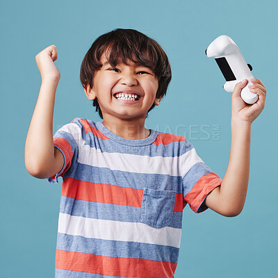 Young mixed race boy standing and holding a console controller while playing a video game against a blue background. cute child celebrating winning a game