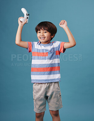 Young mixed race boy standing and holding a console controller while playing a video game against a blue background. cute child celebrating winning a game