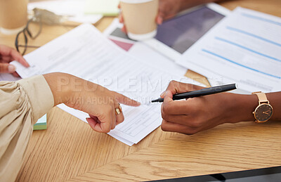 Closeup of two unknown ethnic business woman sitting and signing office contract. Mixed race professional using hand gesture to point on paperwork. African american colleague agreeing to document deal