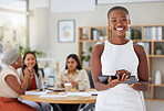 Smiling african american business woman using a digital tablet while colleagues sit behind her in office. Ambitious and happy black professional standing and holding technology while browsing schedule