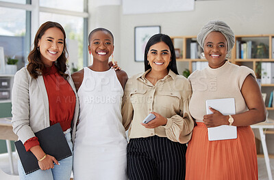 Portrait of diverse group of smiling ethnic businesswomen standing together in office, holding technology and paperwork. Ambitious happy confident professional team of colleagues embracing in support