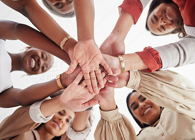 Low angle diverse group of ambitious smiling businesswomen huddled together with hands stacked in middle. Smiling ethnic team of professional colleagues feeling motivated, united, supported and ready