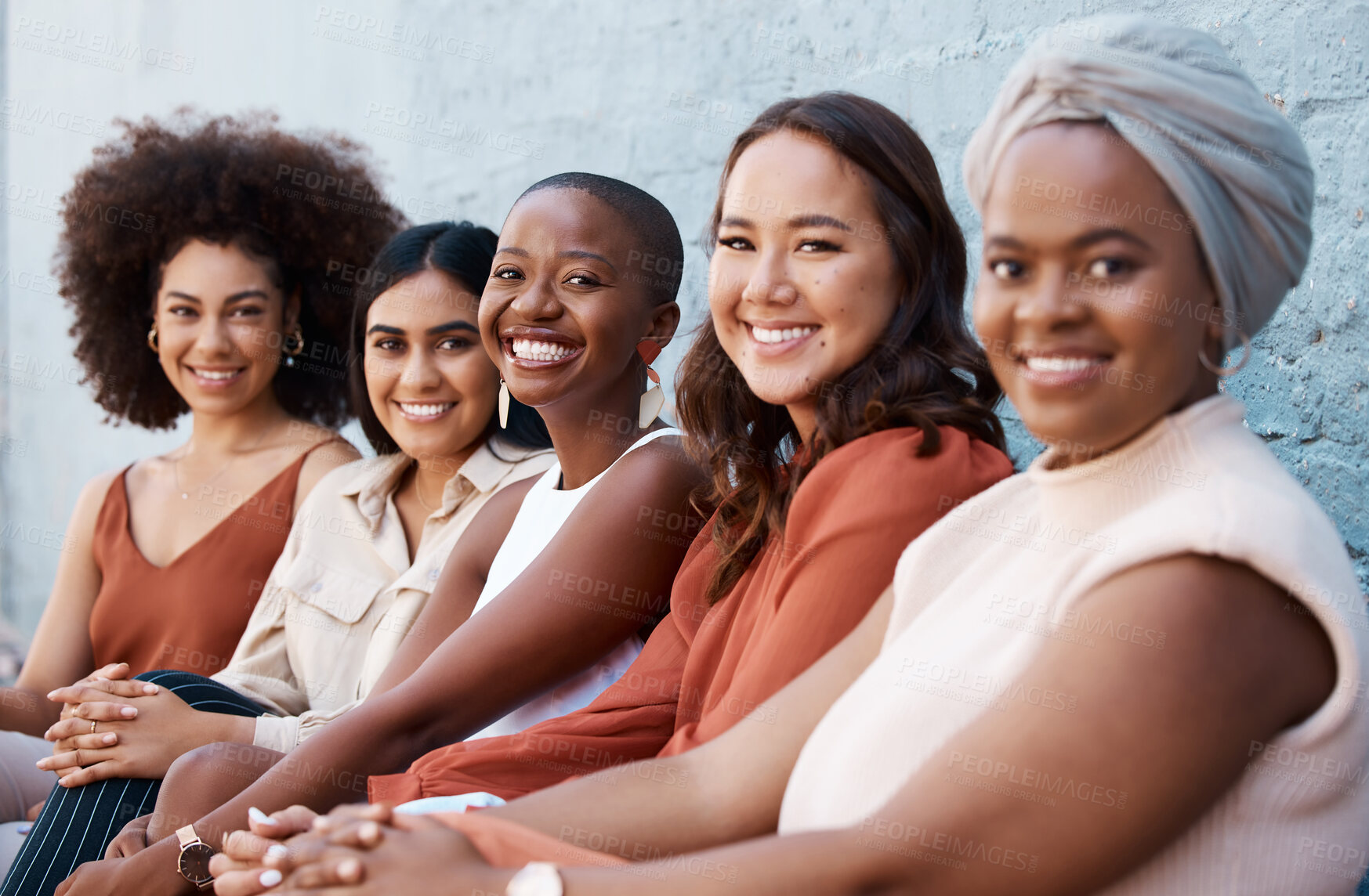 Buy stock photo Portrait, diversity and a group of happy businesswomen sitting in a line as coworkers against a wall outside in the city. Businesspeople smiling while sitting outdoors as woman employee colleagues