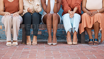 Group of five formal businesswomen sitting on a bench against a wall outside in the city. Legs of friends sitting outdoors on a chair together from below