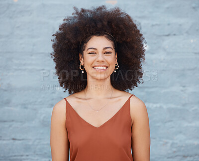 Portrait of cheerful woman with big afro and beautiful smile standing outside against a brick wall. Carefree woman posing outside during the day