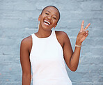 Young african american woman showing a peace sign with her hand smiling and looking happy while standing against a grey wall outside in the city. Peace, love and unity
