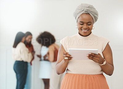 Young confident african american businesswoman holding and using a digital tablet standing in an office at work. Black woman smiling while using social media on a digital tablet