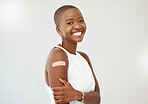 Young african american woman smiling while wearing and showing a bandaid on her arm standing against a white studio background. Happy woman with a plaster on her arm against a white background
