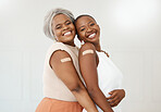 Two young cheerful friends showing a bandaid on their arms standing against a white wall together in an office at work. Happy businesswomen with a plaster on their arms after getting the covid vaccine